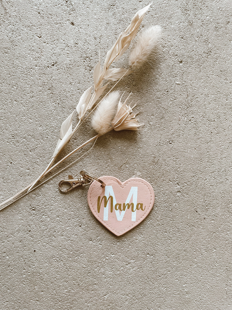 Personalisierter "Mama"-Herz-Schlüsselanhänger liegt neben Trockenblumen auf dem Boden