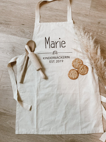 Kinderschürze mit dem Namen "Marie", Holz Kochlöffel, Kekse, Trockenes Weizen auf dem Boden liegend