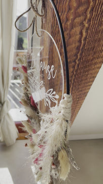 Trockenblumenkranz mit personalisierter "Zuhause" Acrylglasscheibe hängt an einem Holzbalken
