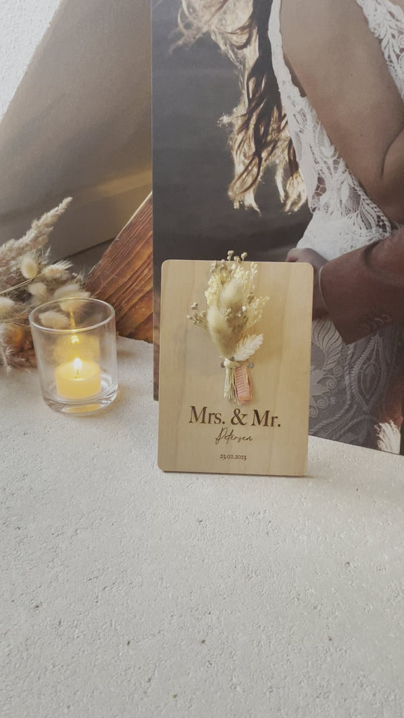 Postkarte aus Holz mit Trockenblumen und einer Personalisierten Gravur, Kerze in einem Glas, Trockenblumen im Hintergrund