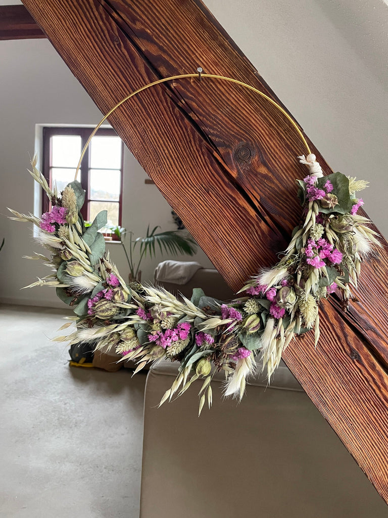 Trockenblumenkranz hängt an einem Holzbalken, Sofa und eine Palme stehen in dem Hintergrund