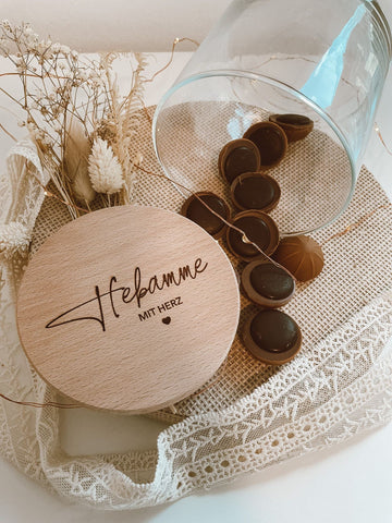 Glas mit toffifee und einem Holzdeckel der "Hebamme mit Herz" eingraviert hat, Trockenblumen