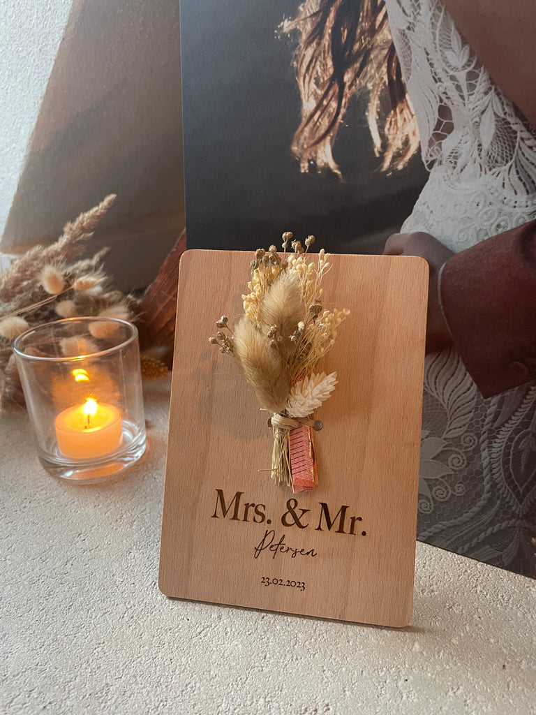 Postkarte aus Holz mit Trockenblumen und einer Personalisierten Gravur, Kerze in einem Glas, Trockenblumen im Hintergrund