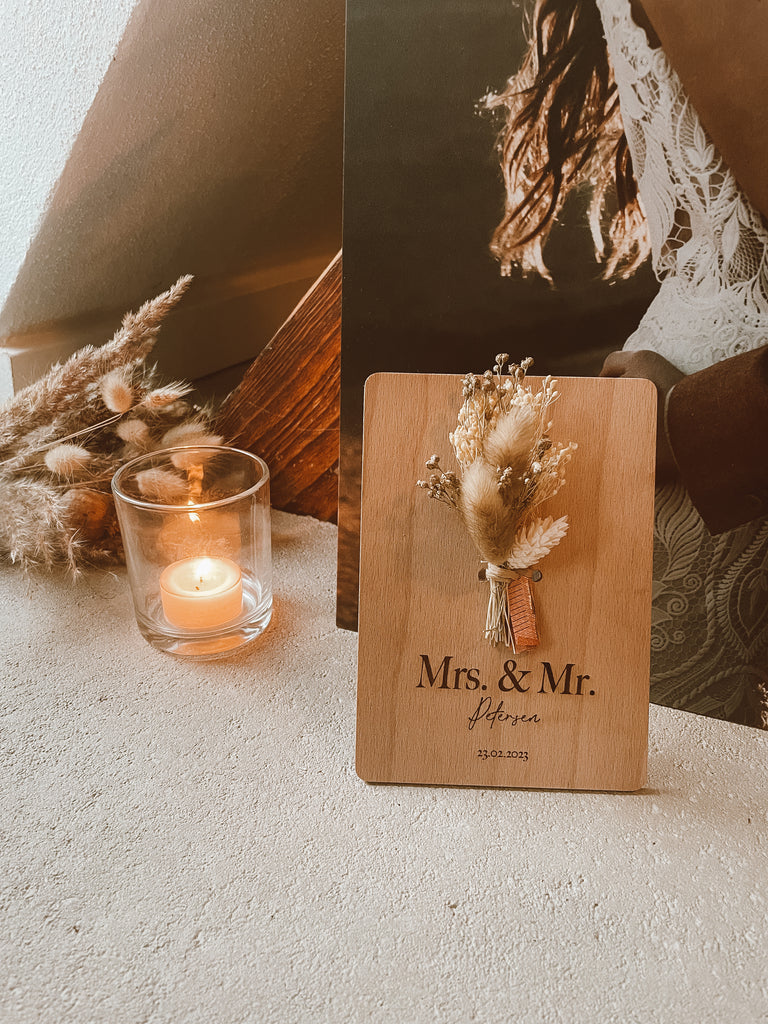 Postkarte aus Holz mit Trockenblumen und einer Personalisierten Gravur, Kerze in einem Glas, Trockenblumen im Hintergrund