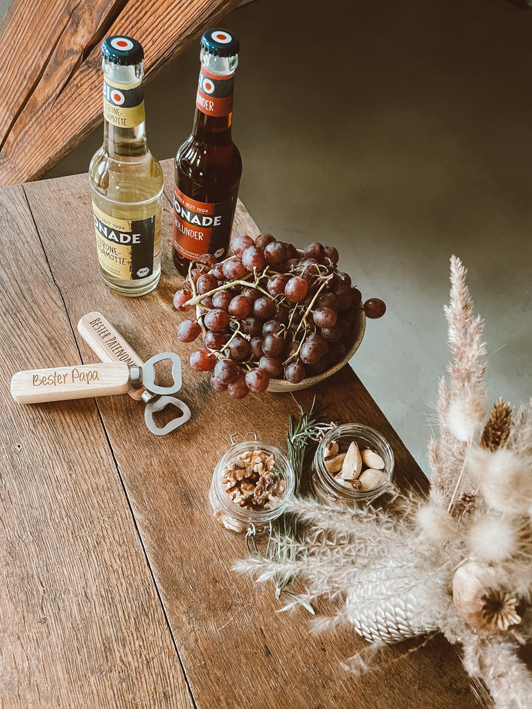 Weintrauben, Bionade, Holz Flaschenöffner mit Gravur, Glasbehälter, Vase mit Trockenblumen, Holztisch, Stuhlbein