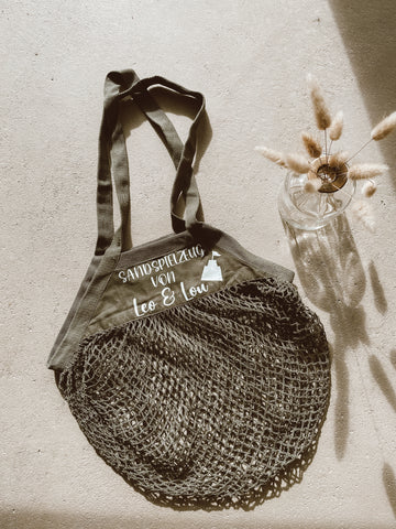 Personalisierte schwarze Sandspielzeugtasche liegt auf dem Boden, Vase mit Trockenblumen