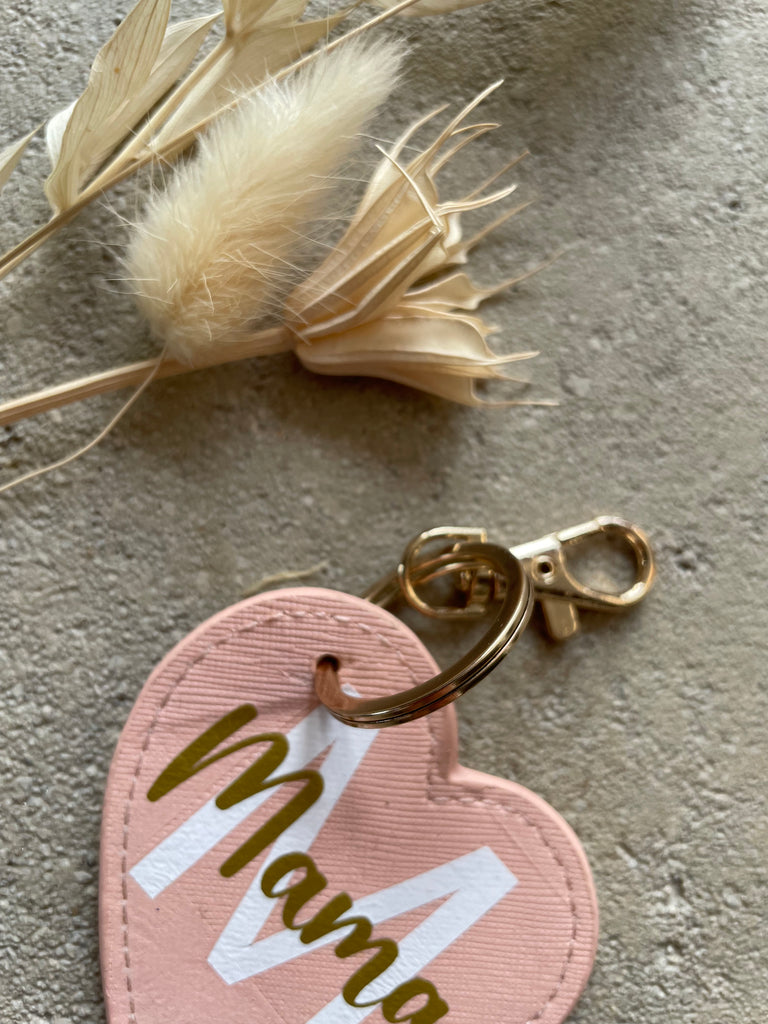Nahaufnahme, Personalisierter "Mama"-Herz-Schlüsselanhänger liegt neben Trockenblumen auf dem Boden
